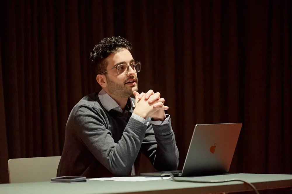 Ein Mann sitzt vor seinem Laptop und spricht.
