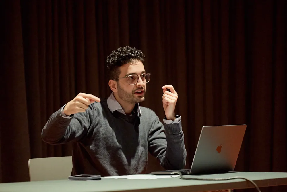 Ein Mann sitzt vor seinem Laptop. Er spricht und gestikuliert mit den Händen.