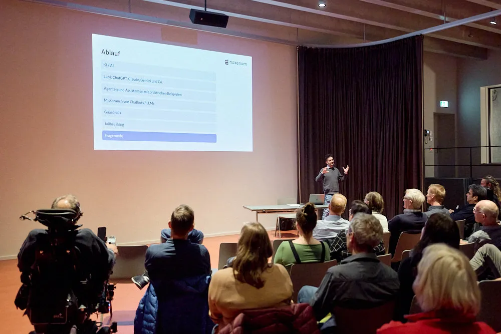 Ein Mann hält vor einem Publikum eine Präsentation. Die Präsentation wird gross an die Wand projiziert.