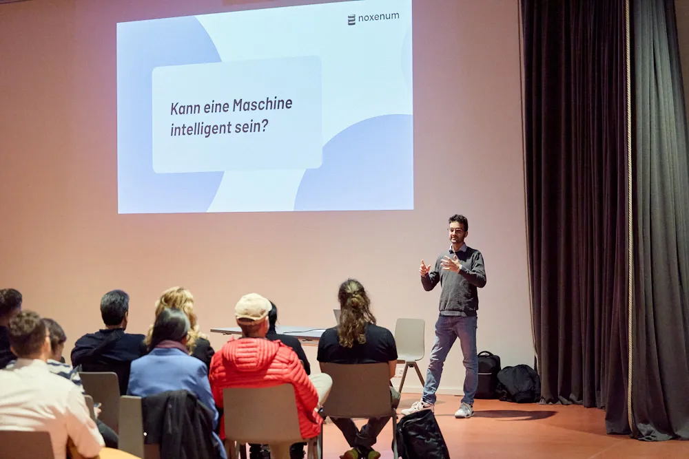 Ein Mann hält vor einem Publikum eine Präsentation. Die Präsentation wird gross an die Wand projiziert.