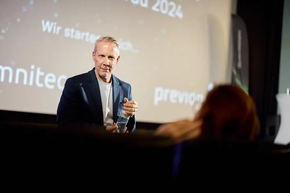 Ein Mann steht vor der Kinoleinwand und lächelt in das Publikum.