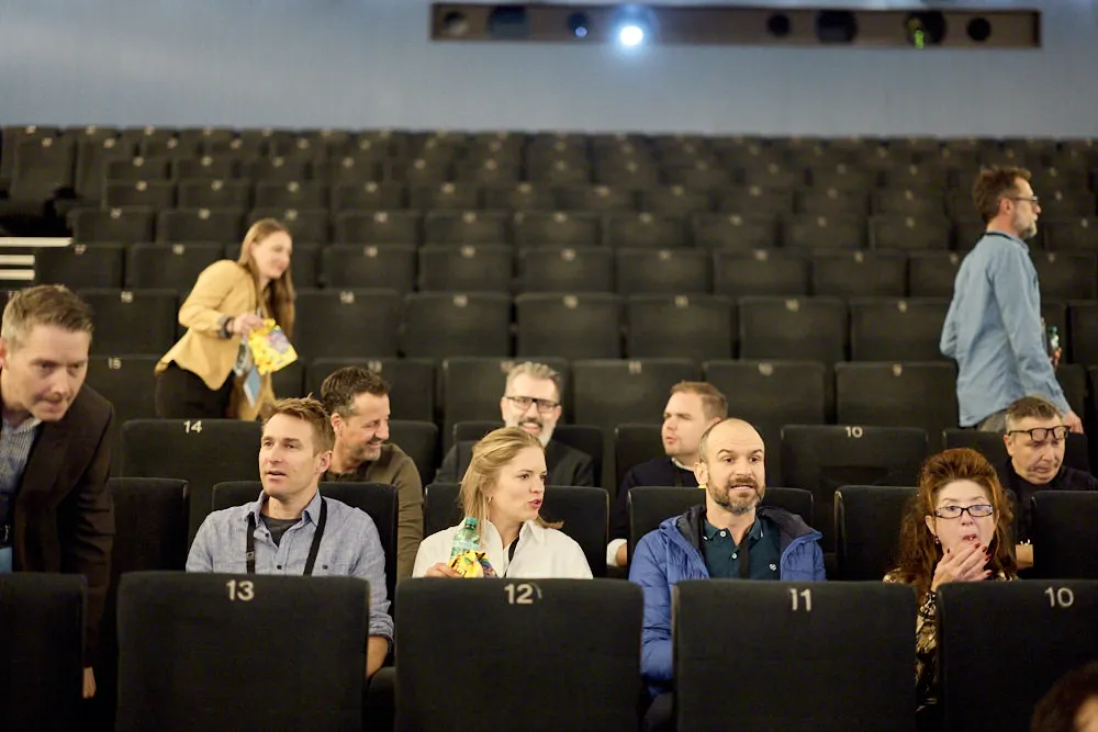 Der Kinosaal füllt sich langsam. Es sitzen bereits verschiedene Personen. Andere Personen suchen ihren Platz.