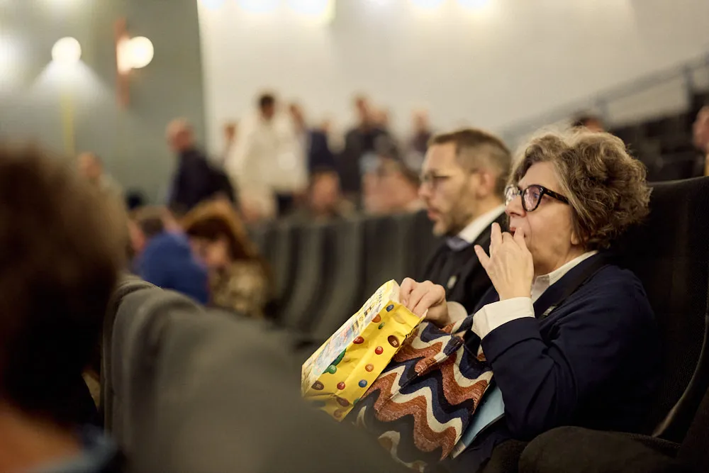 Ein Kinosaal. Im Fokus ist eine Frau. Sie isst Popcorn und schaut gespannt nach vorne.