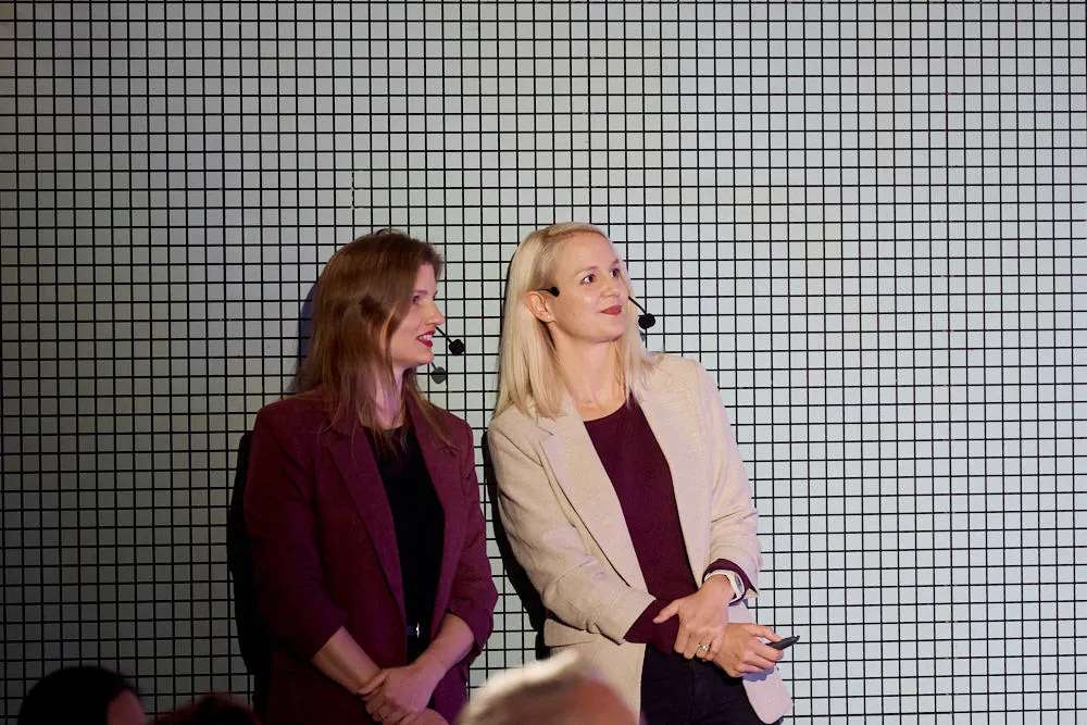 Zwei Frauen mit Headsets stehen nebeneinander und schauen nach schräg oben.