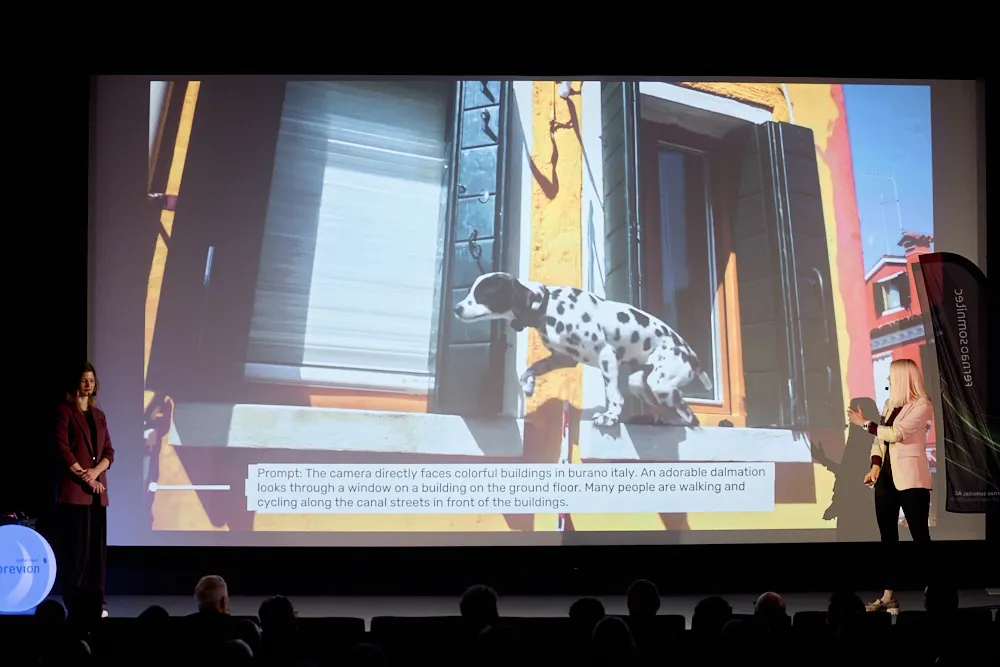 Zwei Frauen mit Headsets stehen vor der Kinoleinwand. Auf der Leinwand wird ein illustrierter Hund, der aus einem Haus springt gezeigt.