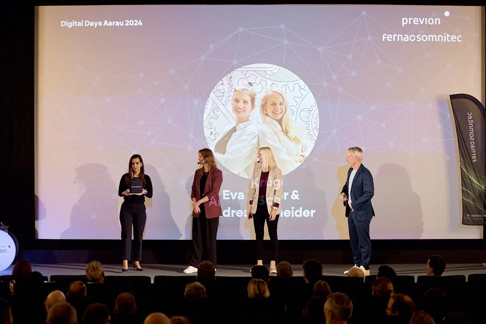 Ein Mann und drei Frauen stehen vor einer Kinoleinwand. Die beiden Frauen in der Mitte tragen beide Headsets. Die Frau links spricht zum Publikum.