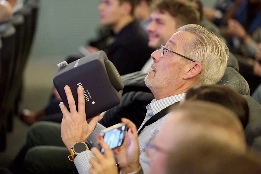 Ein Mann im Publikum hält ein Stoffwürfel mit Logo drauf in den Händen. Er sieht erstaunt aus.