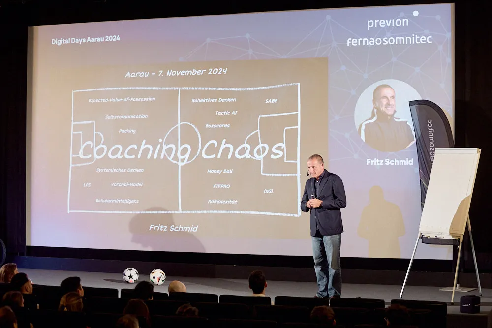 Ein Mann steht vor der Kinoleinwand und spricht zum Publikum im Kinosaal. Auf der Leinwand wird seine Präsentation projiziert.