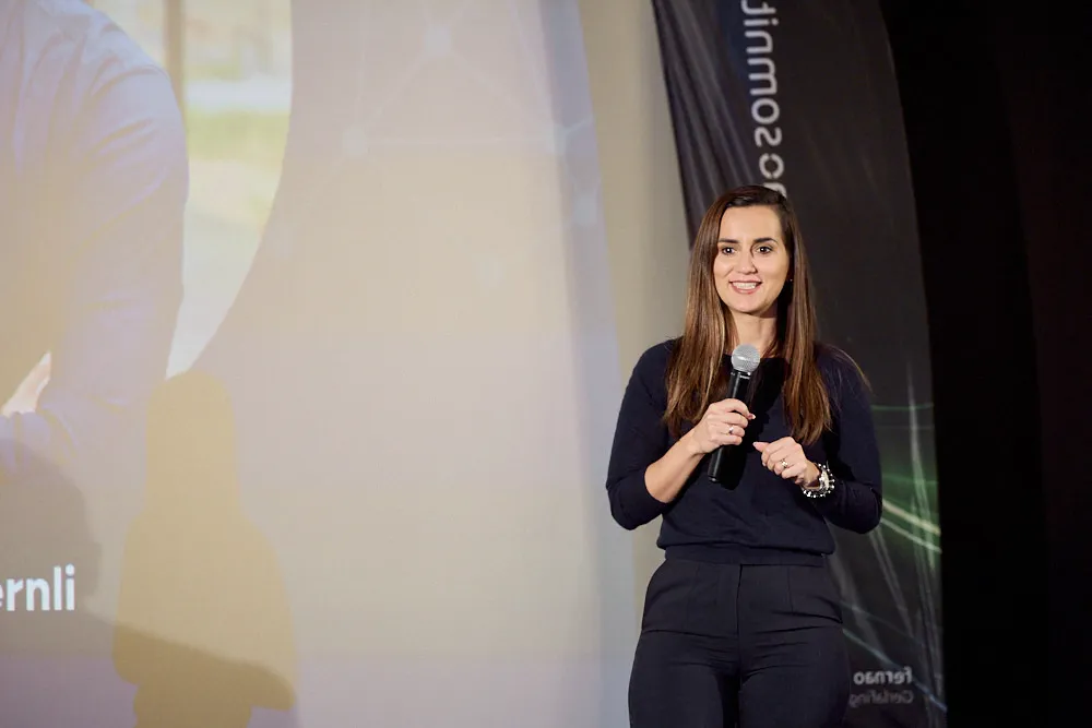 Eine Frau spricht vor einer Kinoleinwand in ein Mikrofon. Sie lächelt.