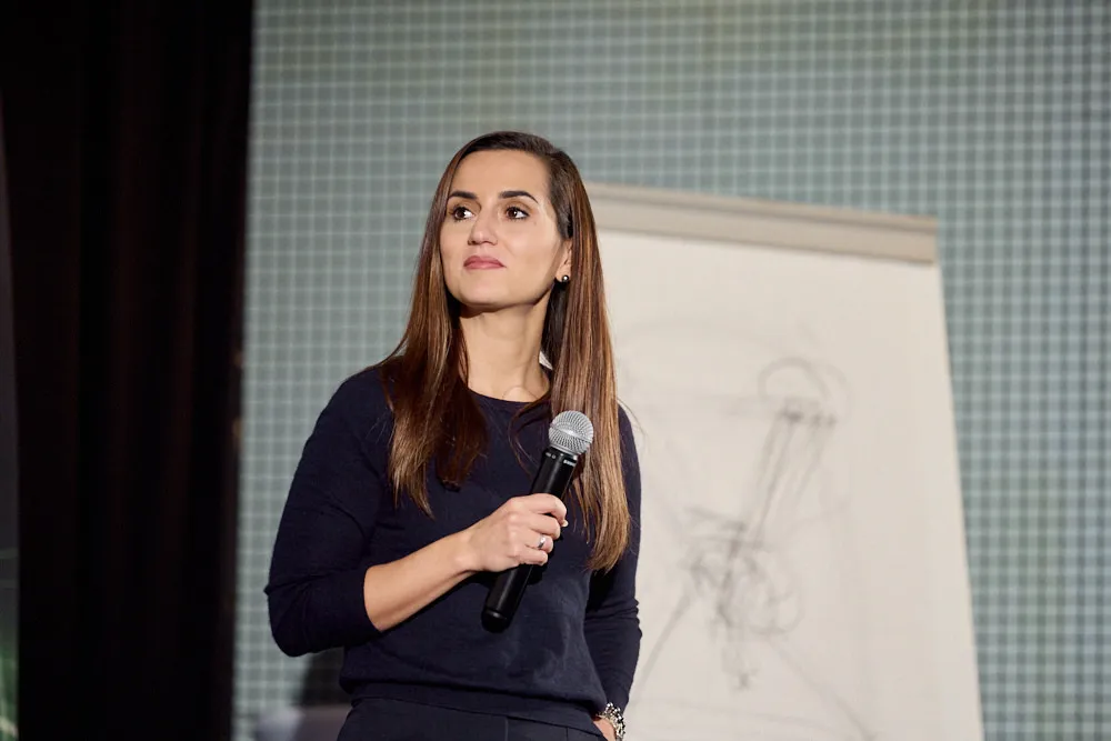 Eine Frau mit einem Mikrofon vor einem Whiteboard. Sie schaut auf die Seite.