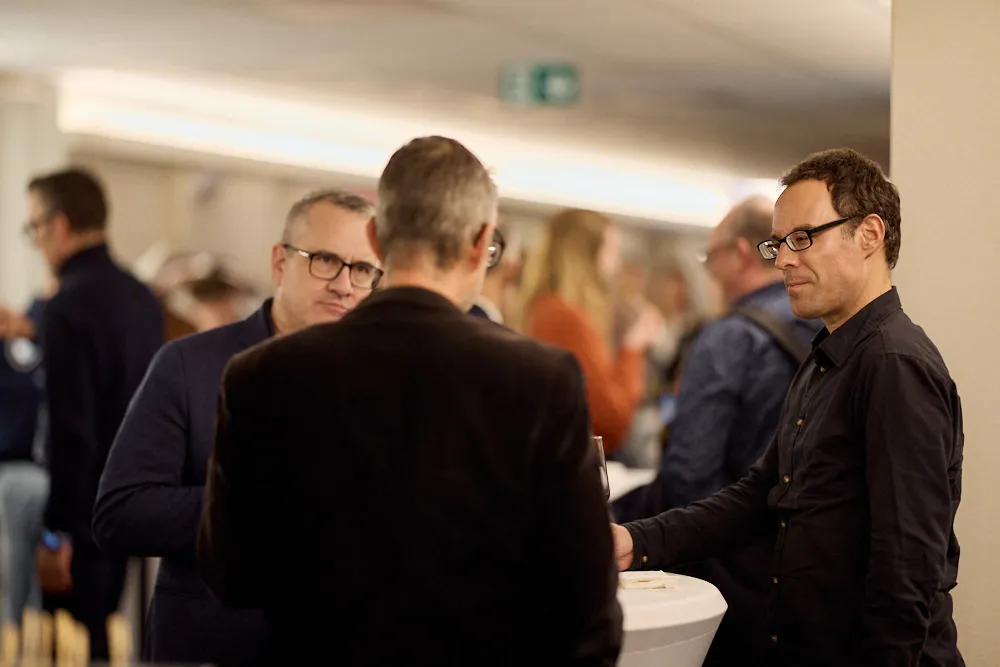 Drei Männer sprechen an einem Stehtisch miteinander.