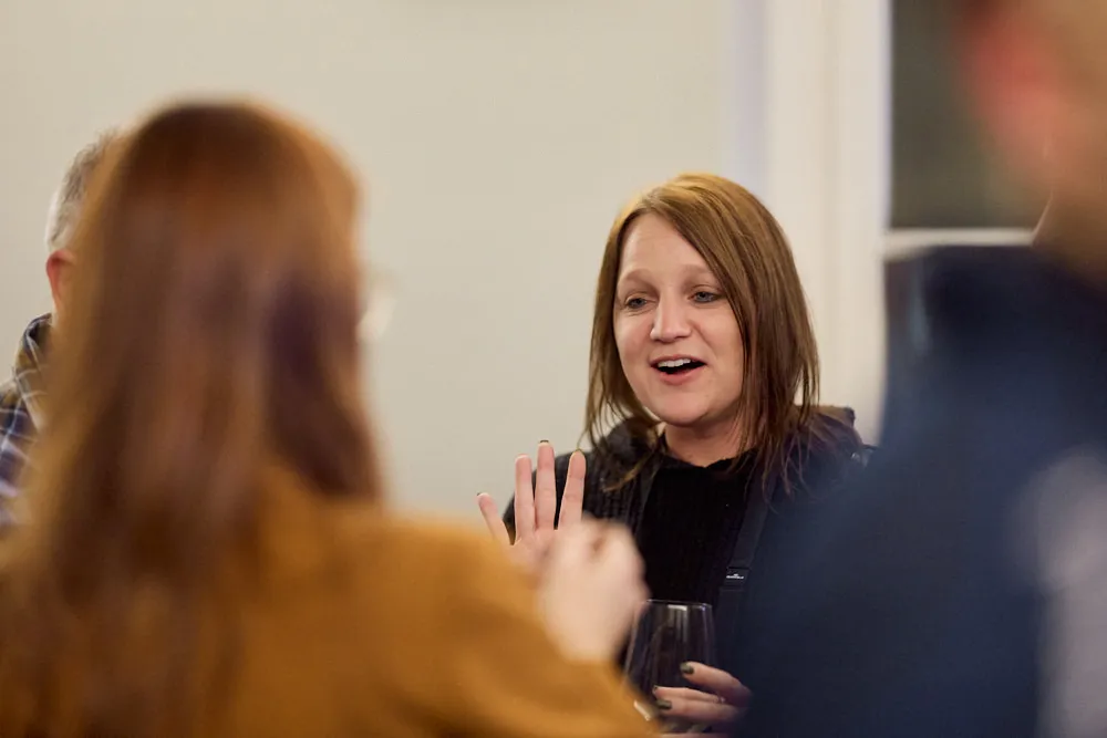 Ein Mann und zwei Frauen unterhalten sich. Der Fokus liegt auf der sprechenden Frau. Sie hält eine Hand hoch..
