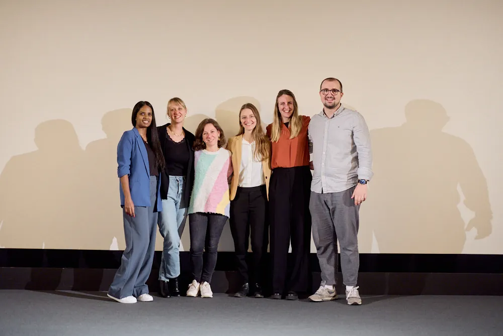 Ein Mann und fünf Frauen stehen vor der Kinoleinwand. Sie lächeln alle.