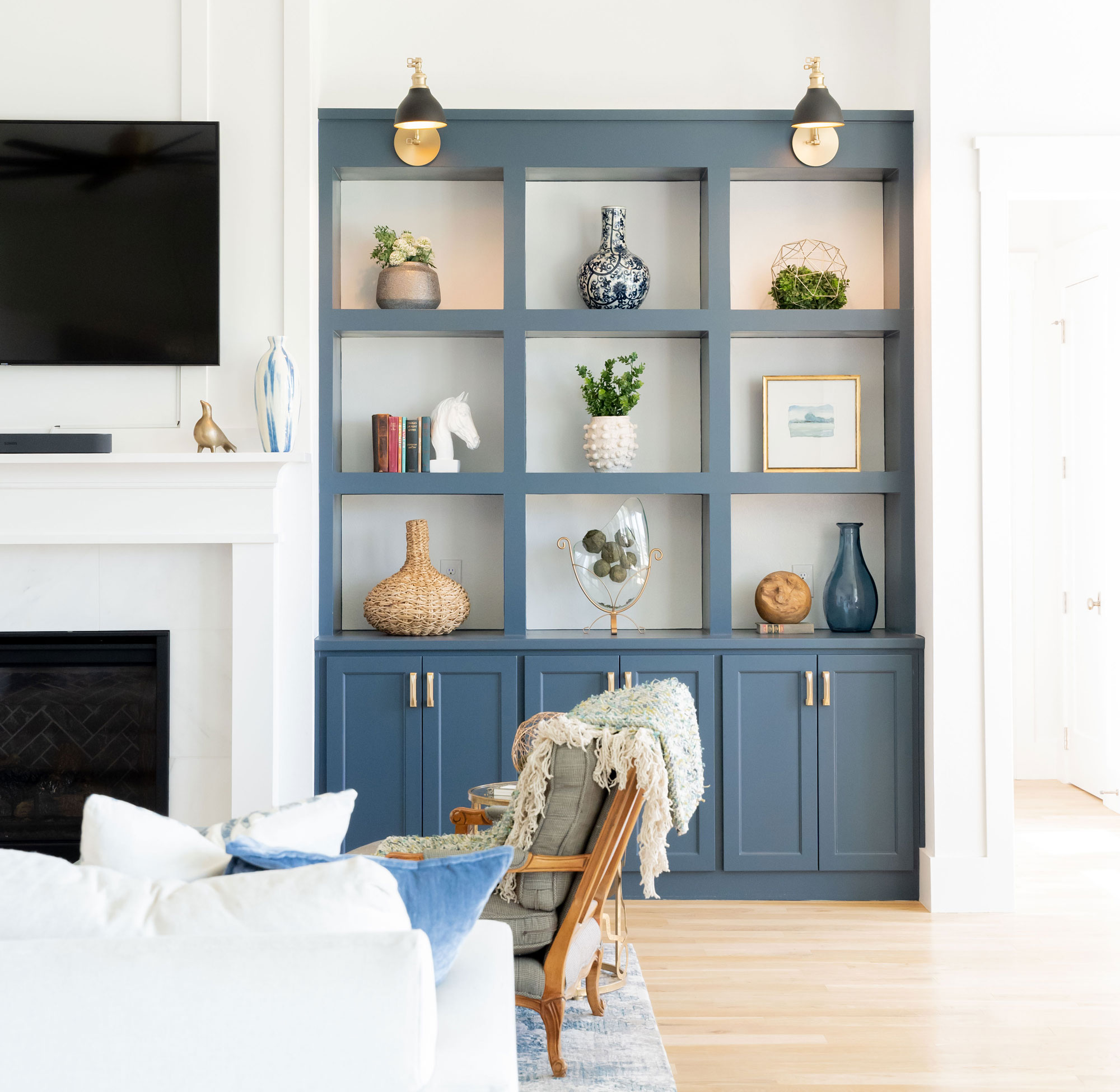 Blue built-in shelves with plants and decorative items, next to a white fireplace and wall-mounted TV.