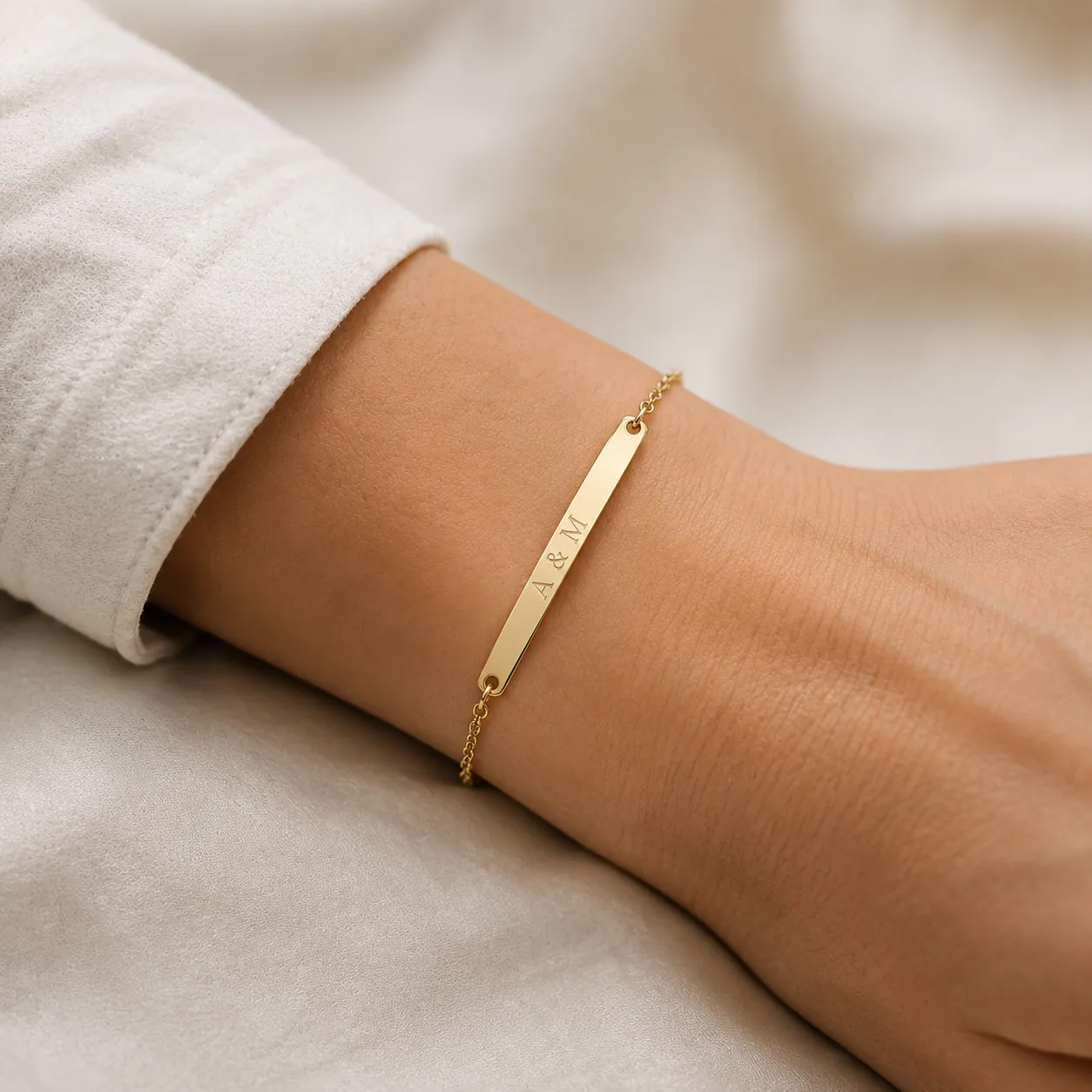 Gold bar bracelet engraved "A & M" worn on a wrist