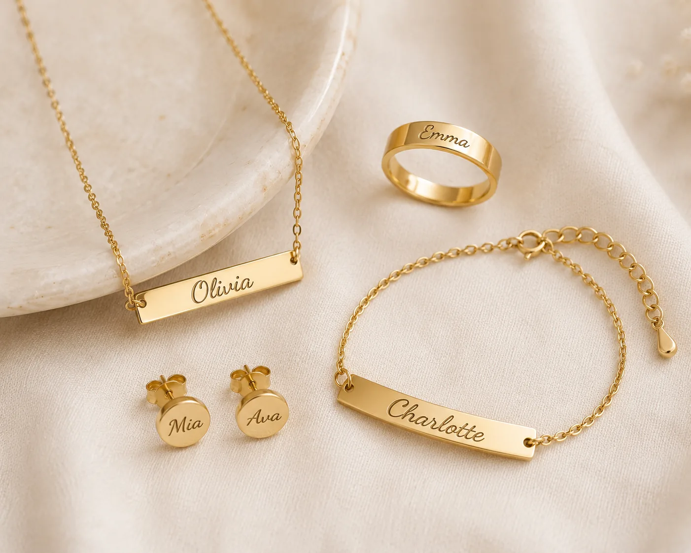 Gold jewelry set with engraved names: a necklace reading "Olivia," stud earrings "Mia" and "Ava," a bracelet "Charlotte," and a ring "Emma"