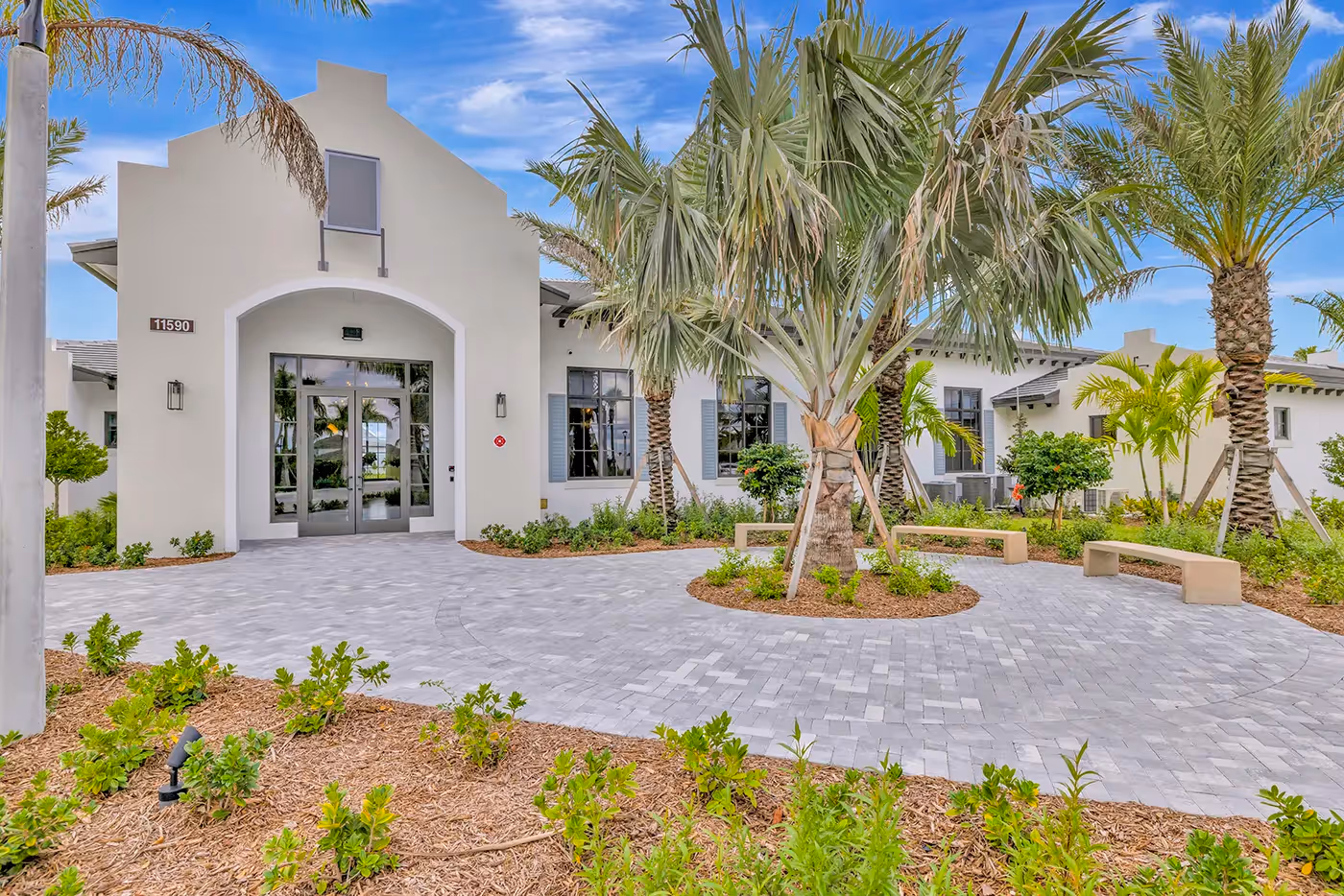 Exterior of the modern clubhouse and leasing center, featuring a welcoming paved entrance and palm trees at Alton Central Park in Port St. Lucie, FL.