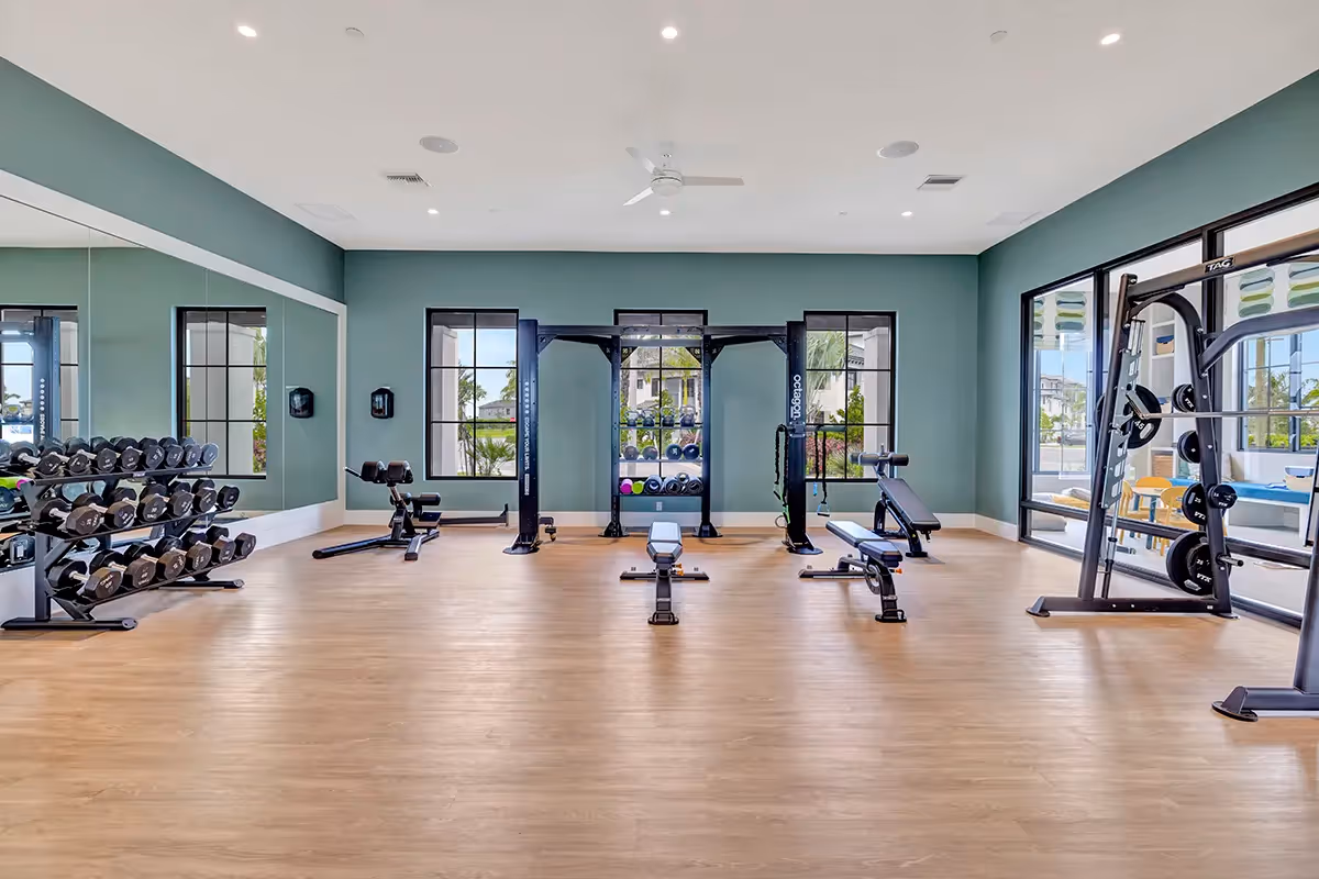 Weight training section of the resident fitness center, featuring free weights, benches, and strength equipment against a calming green accent wall at Alton Central Park in Port St. Lucie, FL.