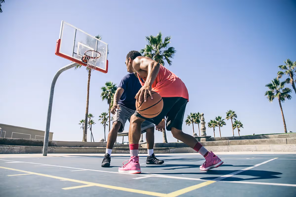 Two men playing basketball on a sunny outdoor court surrounded by palm trees, showcasing the community's recreational amenities in Port St. Lucie, FL.