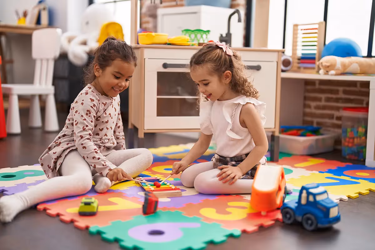 Two young girls playing with toys on a colorful floor mat, representing the family-friendly community environment at Alton Central Park in Port St. Lucie, FL.