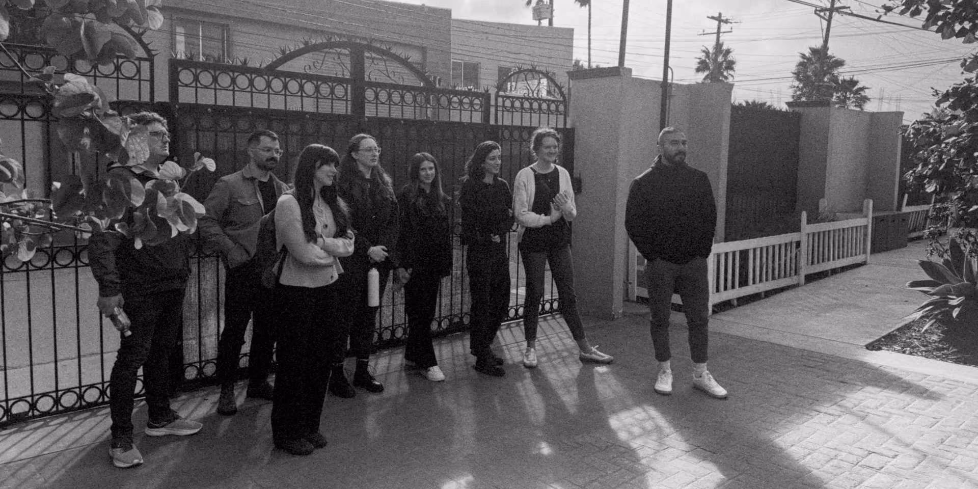 Black and white grainy side view of team standing in front of a gate looking away