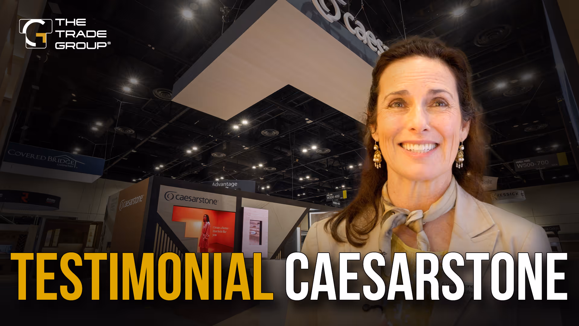 Smiling woman in light blazer at a trade show booth with Caesarstone and The Trade Group logos.