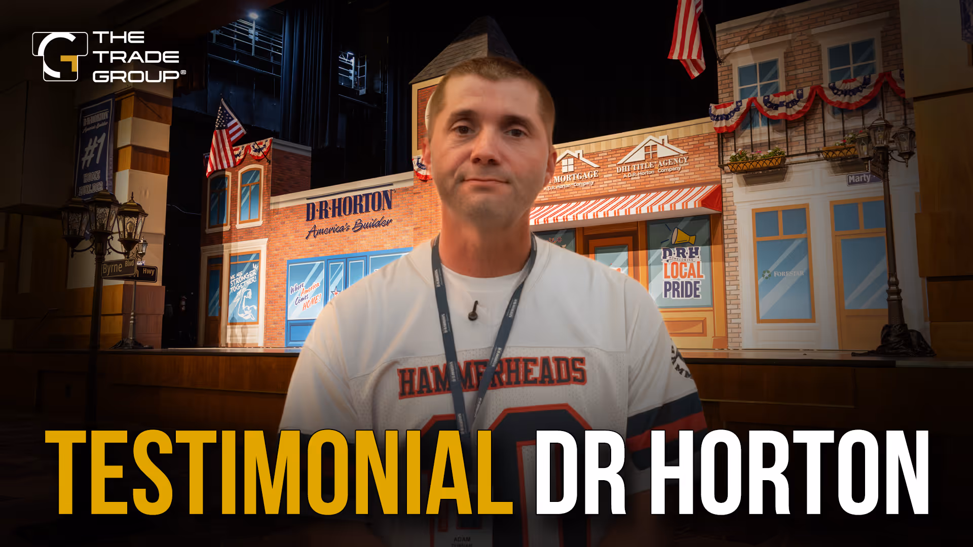 Man wearing a Hammerheads jersey stands in front of a D.R. Horton building backdrop with patriotic decorations.