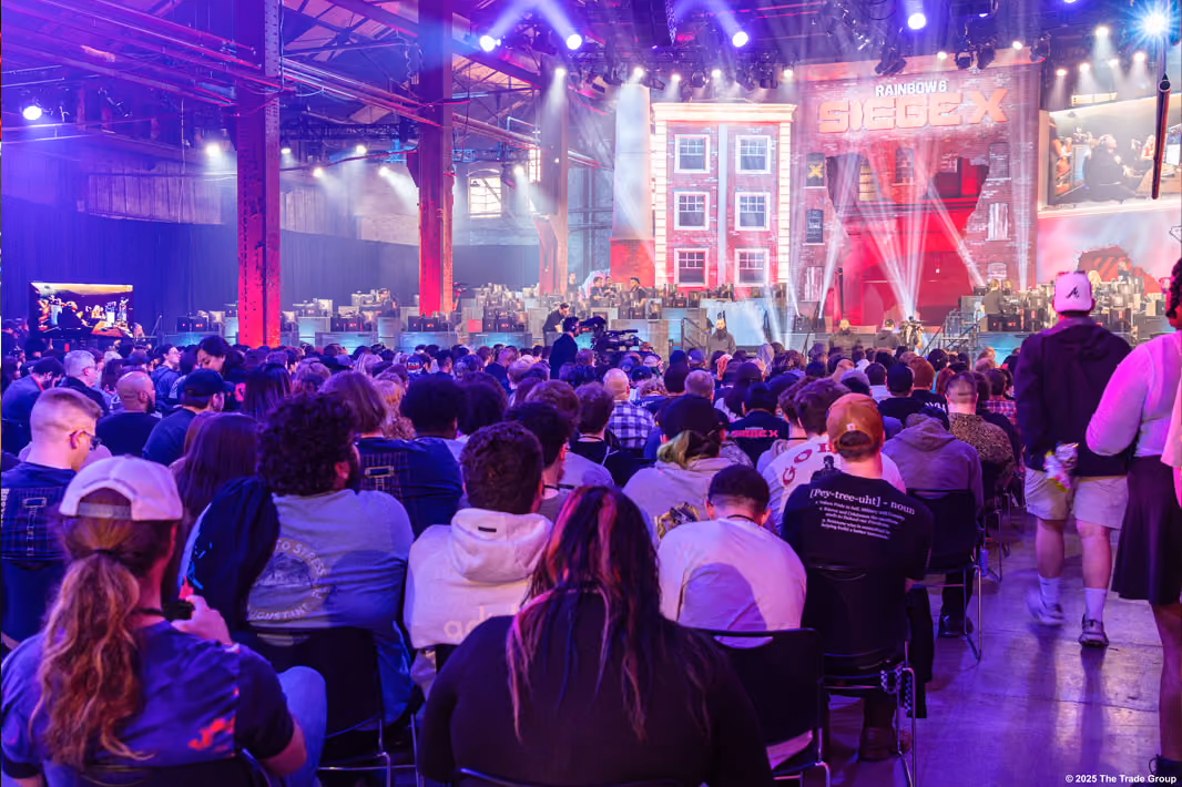 Crowd at Rainbow Six Siege X esports event with players on stage under purple lighting.