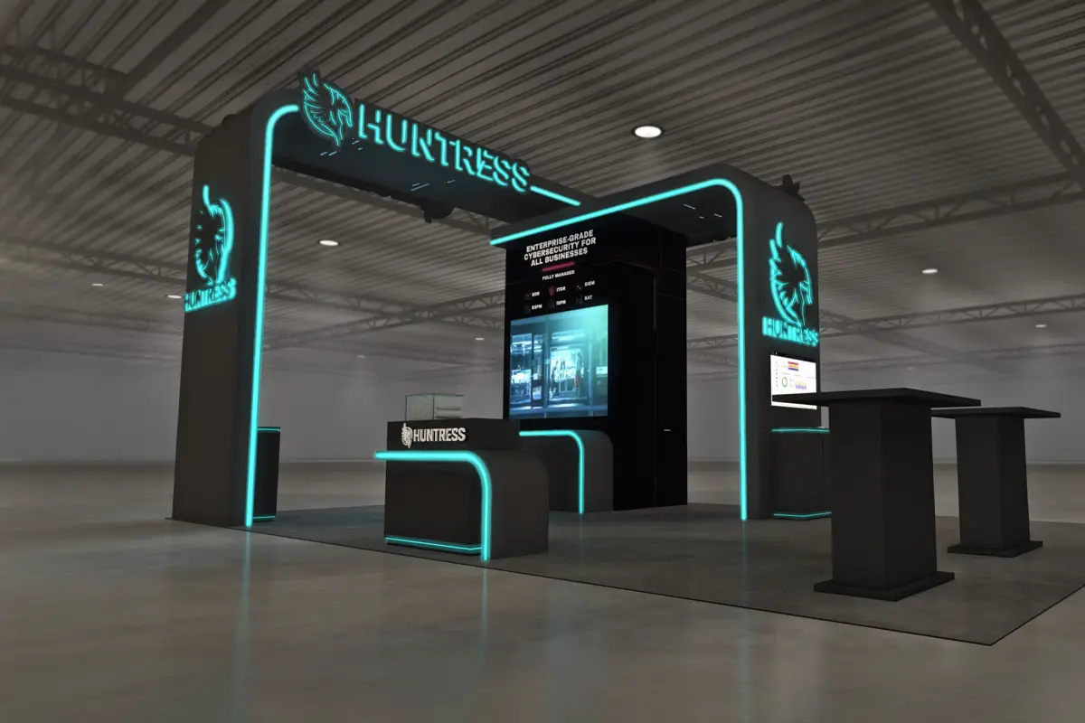 Cybersecurity trade show booth with neon blue HUNTRESS logo and displays in a large hall.
