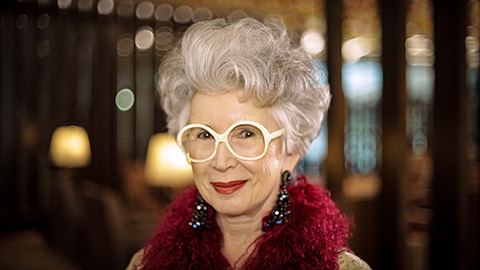 glamorous older woman in white glasses and a red boa, Emirates commercial