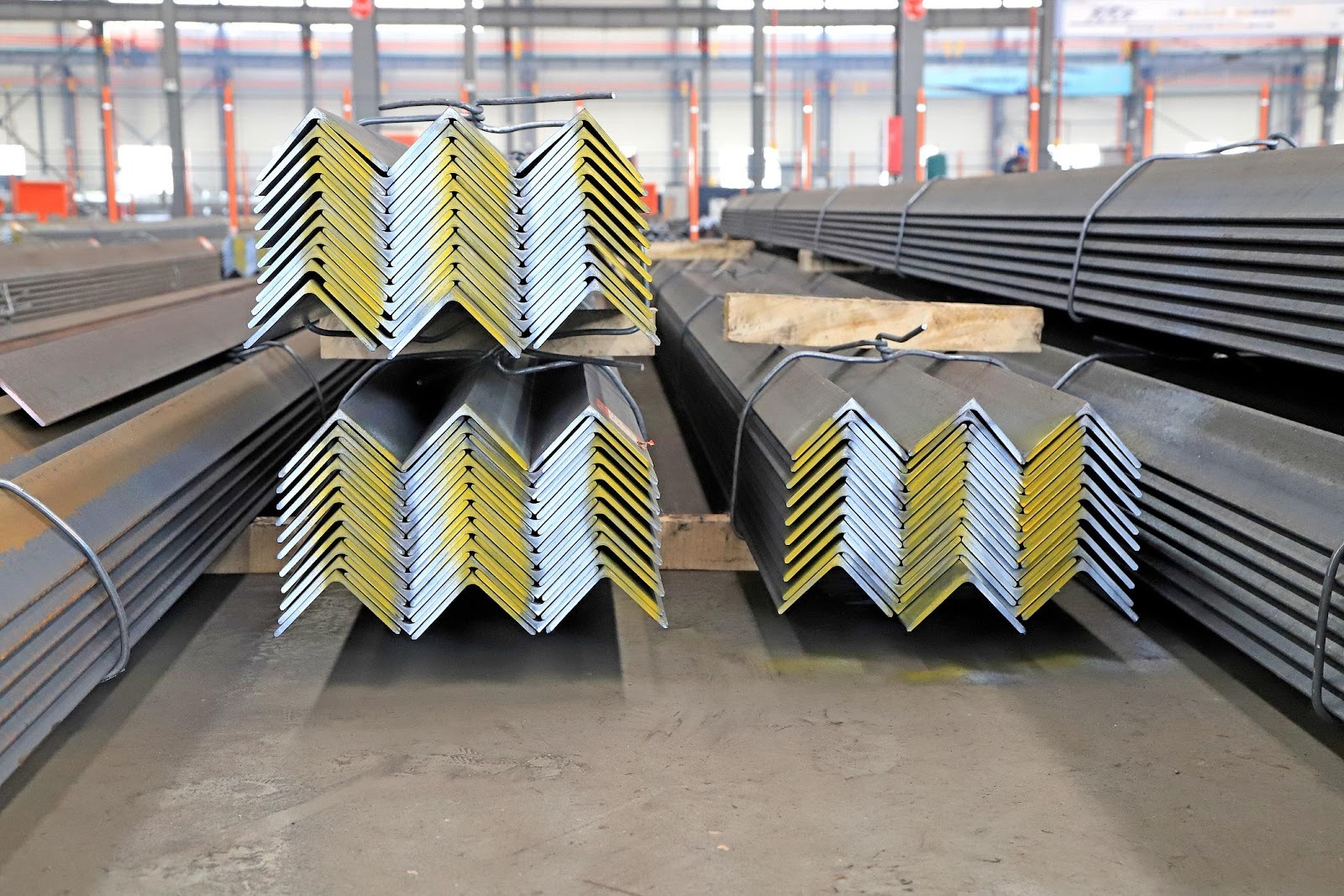 Perfiles ángulo de acero apilados ordenadamente en bodega industrial techada.