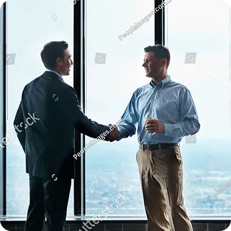Two men shaking hands in an office with large windows and city view in the background.