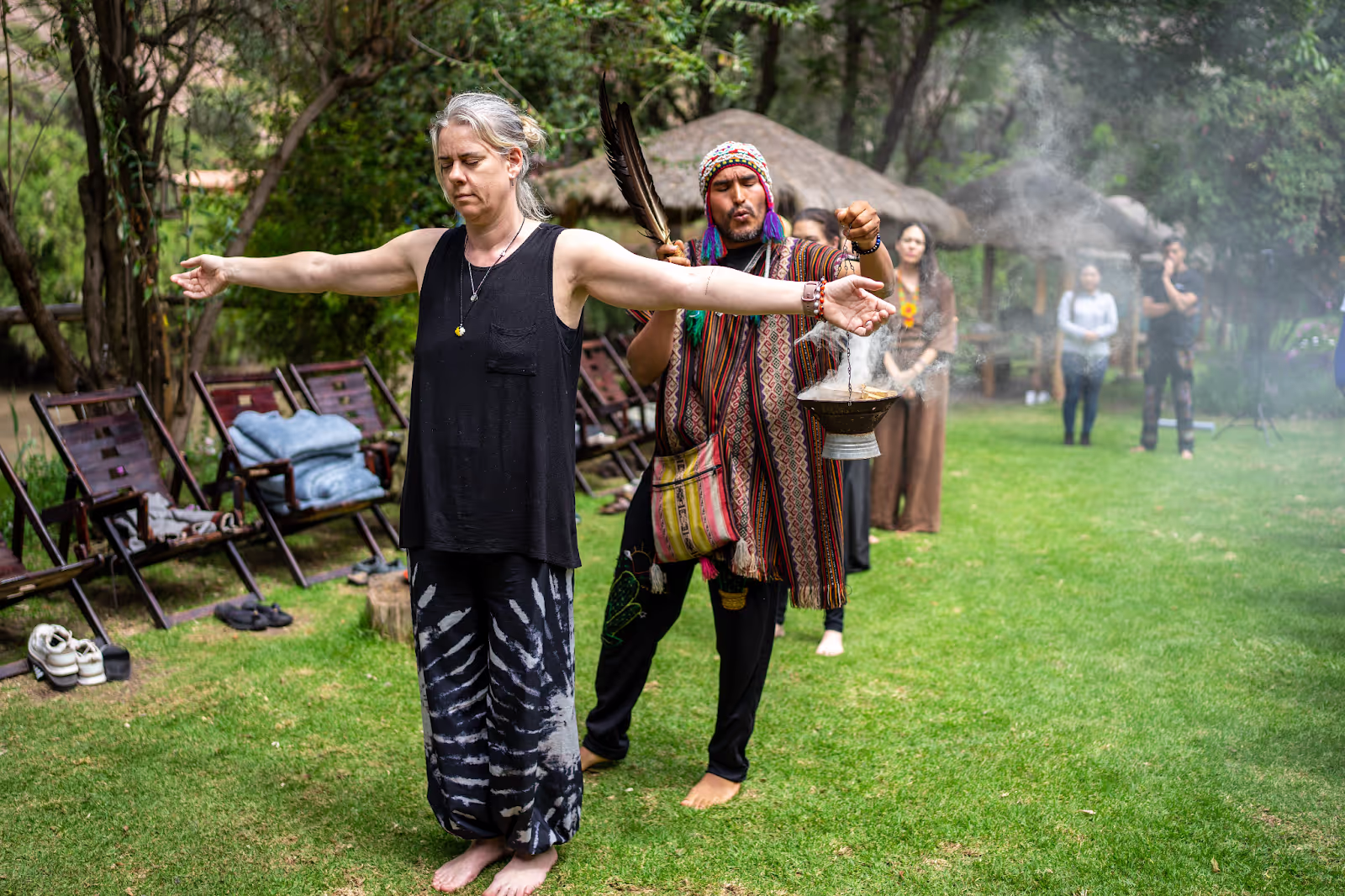 A woman in a black outfit with outstretched arms participates in a cleansing ceremony.