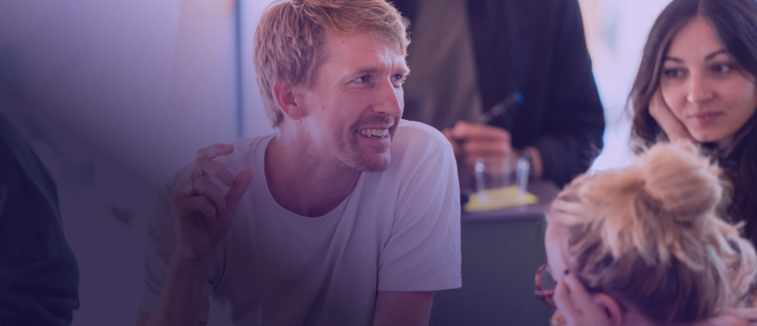 Ein Mann, der in einem interaktiven Diskussionskreis, umgeben von Gleichaltrigen in einem Lernraum, eine Idee teilt.