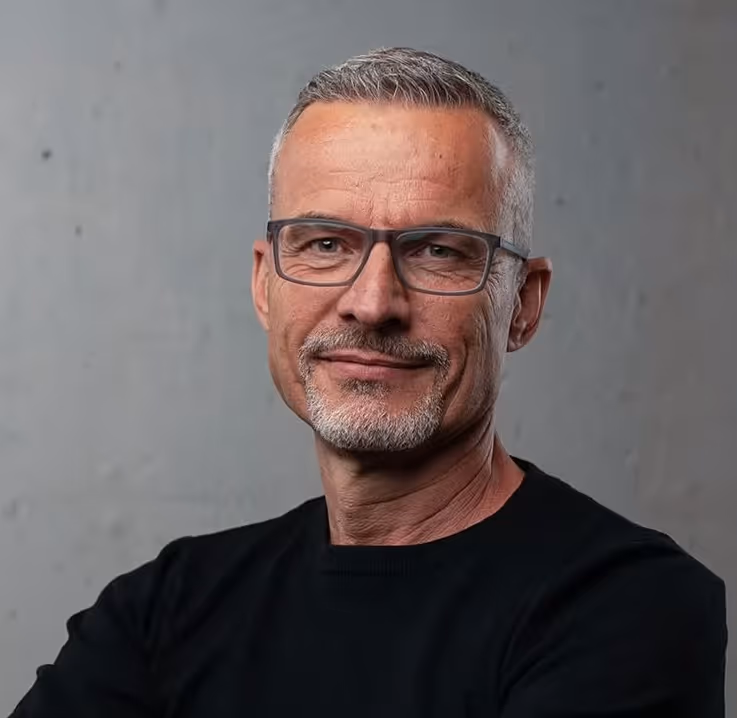 Middle-aged man with short gray hair, glasses, and a gray goatee wearing a black shirt.