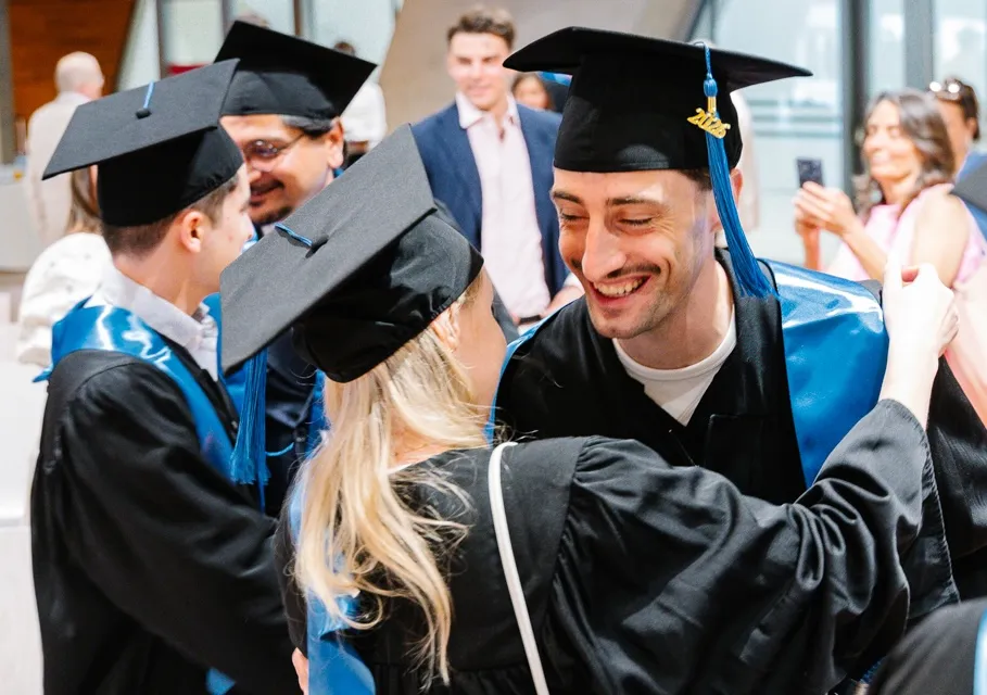 Graduates in black caps and gowns smiling and greeting each other at a graduation ceremony.