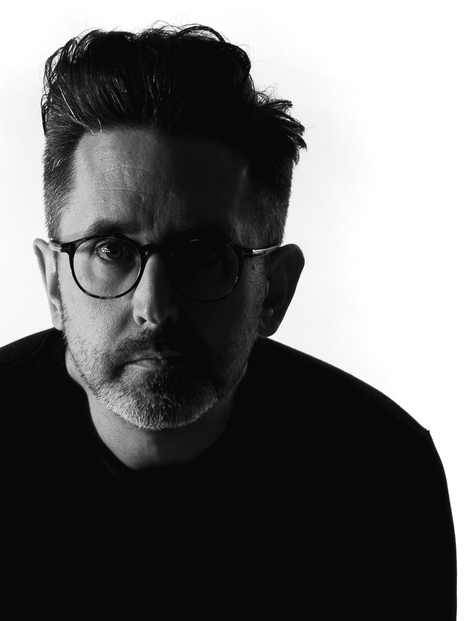 A high-contrast, black and white photo of Adam looking directly at the camera.