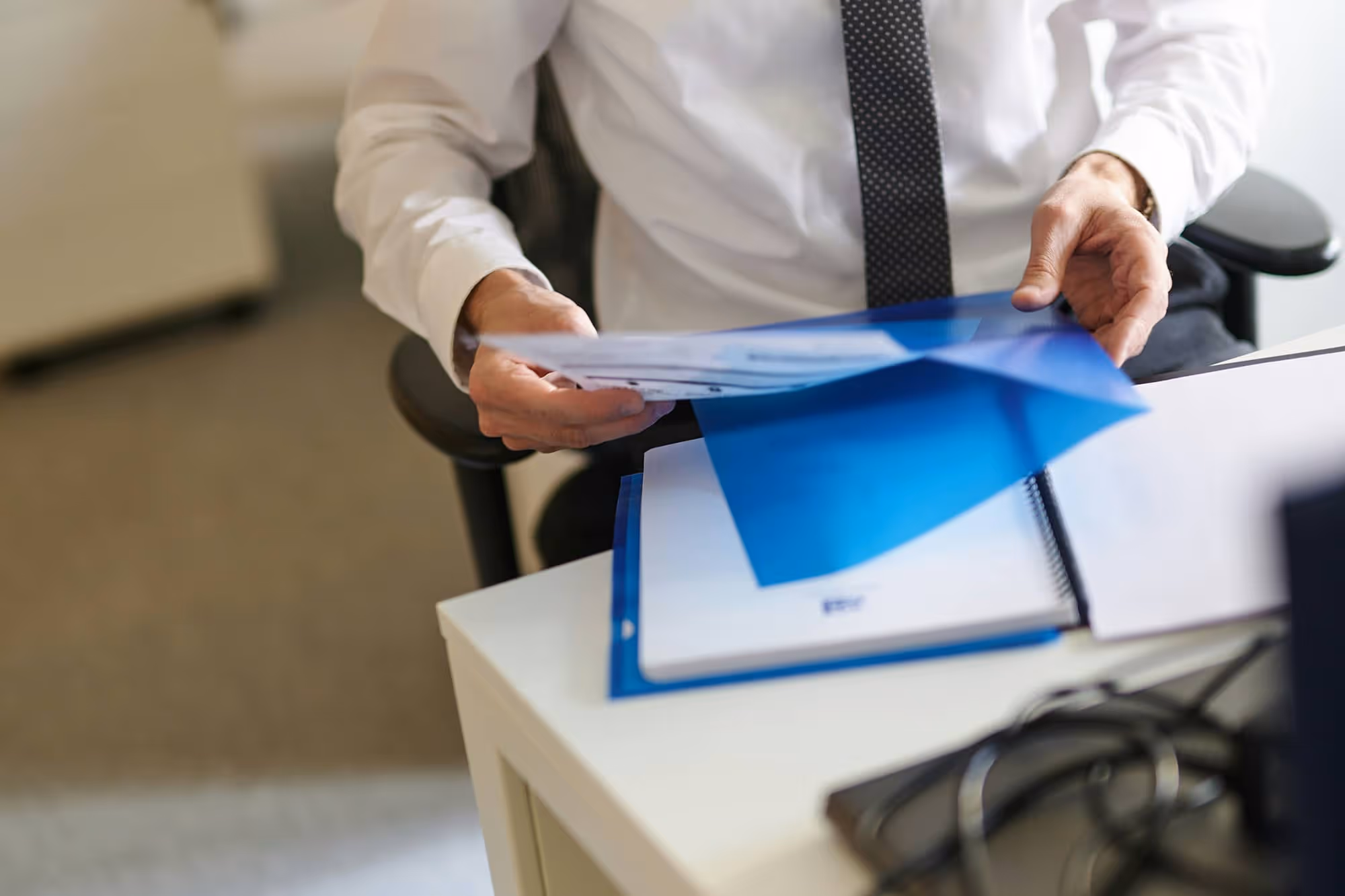 A Businessman Sitting Behind The Table Holding A Folder