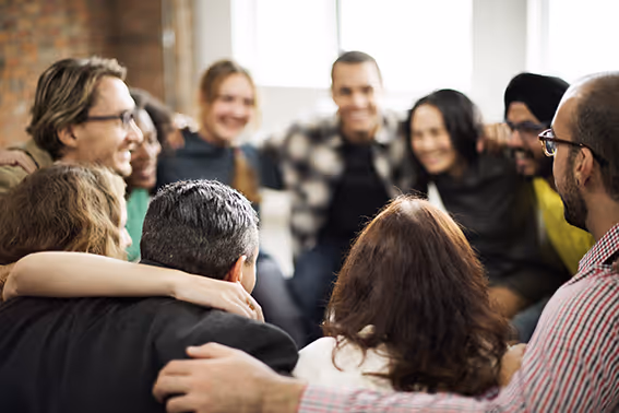Group of people gathered in a circle with their arms around each other at a community wellness event.