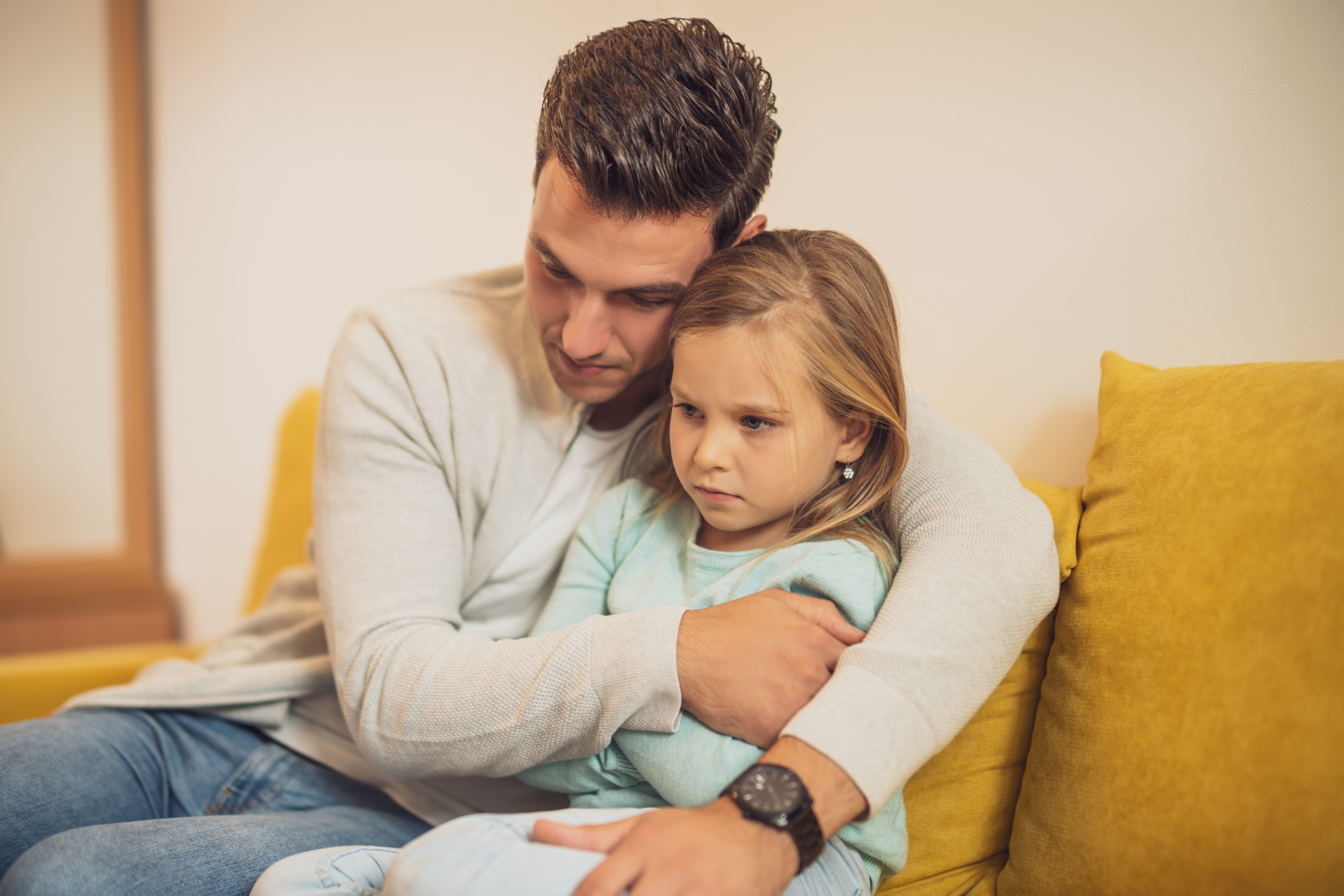 Father holding young daughter sitting on couch