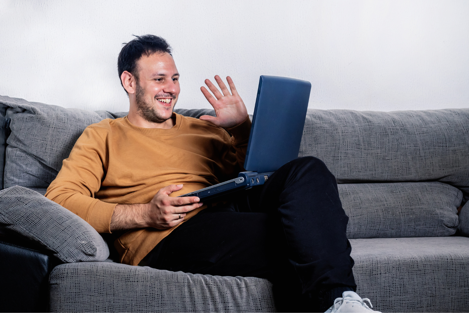 Man sitting on couch on video call attending telehealth appointment and smiling