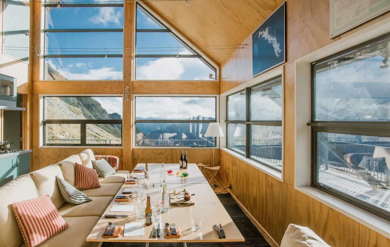 Bright dining room with large windows showing mountain views, a long table, and cushioned seating.
