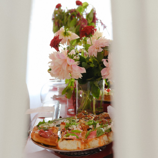 Plate of pizza slices next to a vase with pink and red flowers on a table.