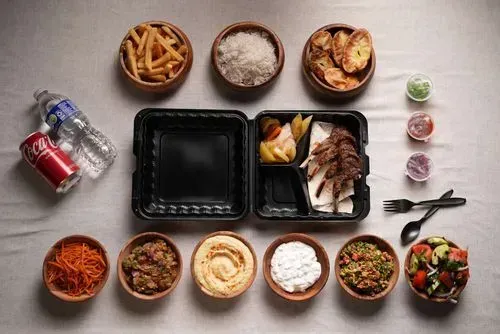 Lamb chops served with a variety of sides including rice, potato wedges, fries, hummus, tabbouleh, coleslaw, and a bottle of water and soda.