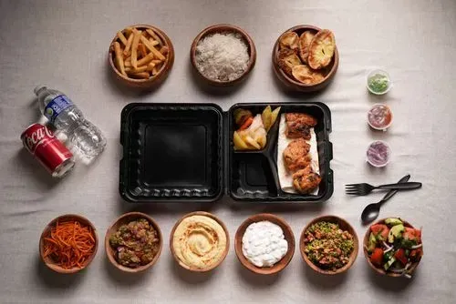 Grilled pork BBQ served with potato wedges, rice, fries, hummus, tabbouleh, coleslaw, and a bottle of water and soda.