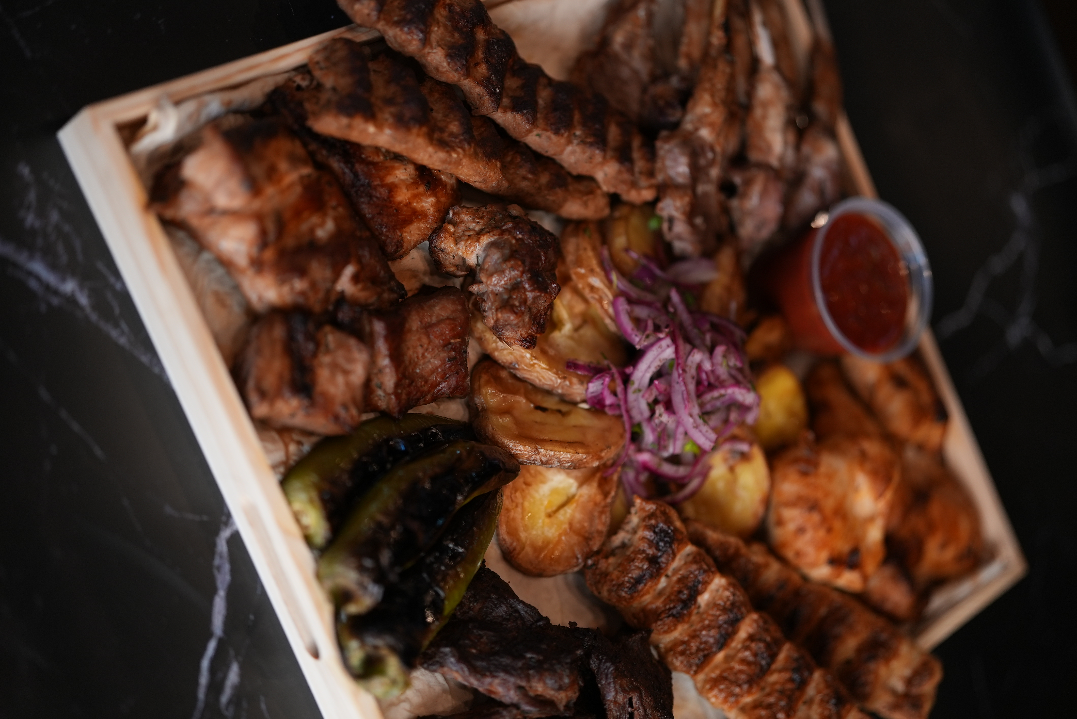 Large BBQ platter for twelve people with a variety of grilled meats, vegetables and roasted potatoes, garnished with red onions.