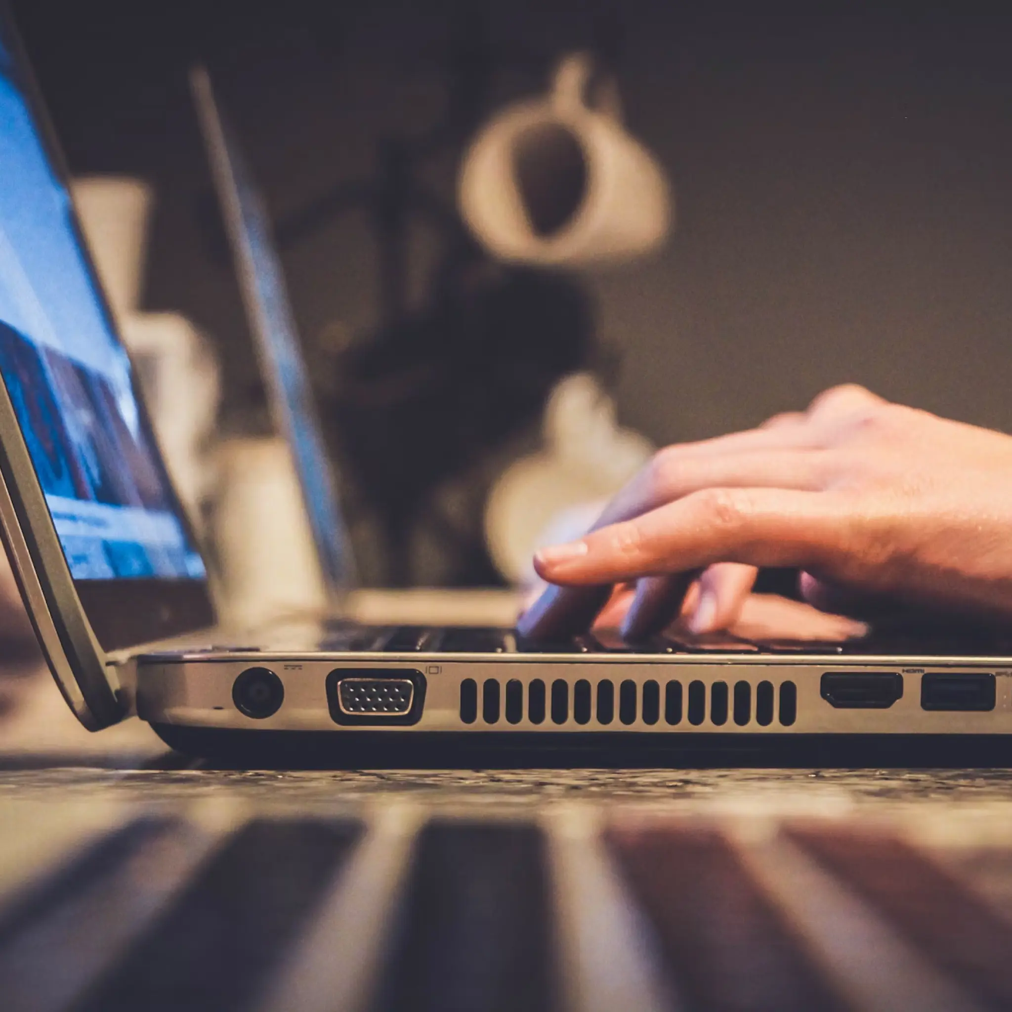 Close-up of hands typing on a laptop keyboard on a reflective surface with blurred background.