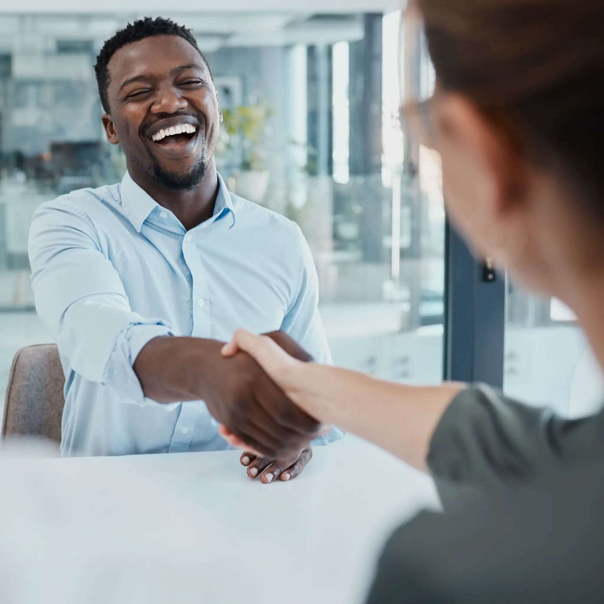 Smiling man in blue shirt shaking hands with a woman in an office setting.