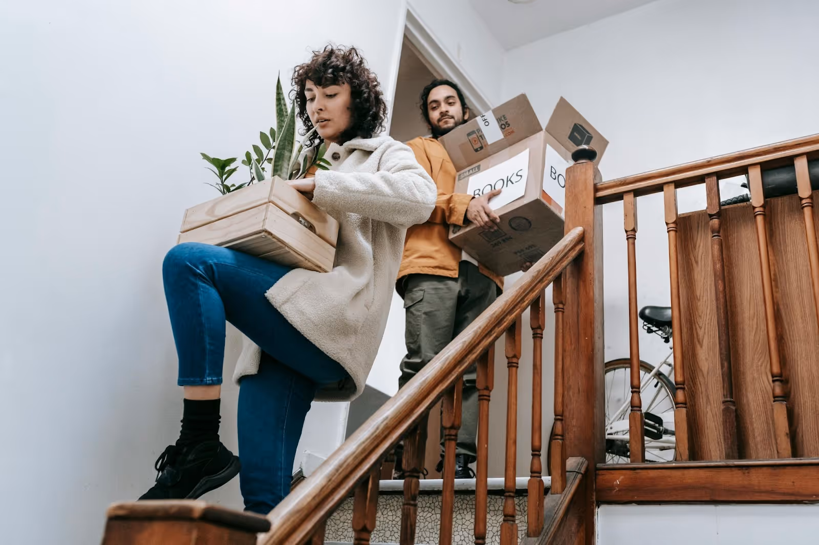 Couple moving boxes while walking down carpeted and wooden stairs