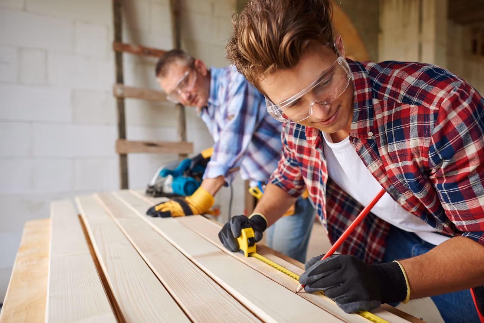 Two carpenters working together on measuring wooden planks